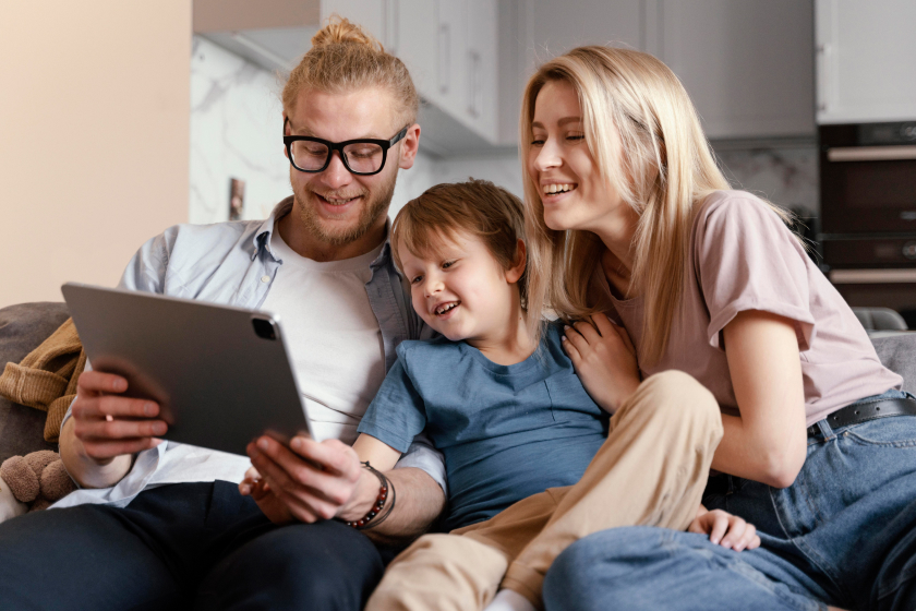 Happy parents with their child using a tablet to explore parenting apps at home.